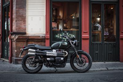 A Triumph Street Scrambler parked on a street outside a cafe